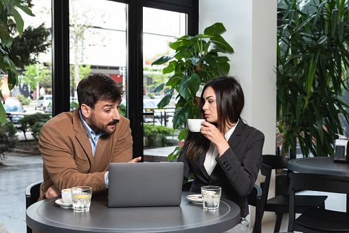 Two young business people having a successful meeting at restaurant. Businessman and businesswoman sitting in cafeteria working together on laptop computer