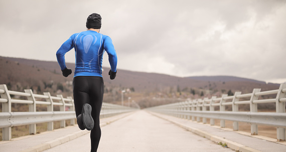 Rear shot of a man in sports outfit running on a bridge