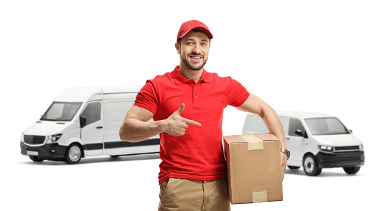 Delivery guy pointing at a box in front of trasnport vans isolated on white background