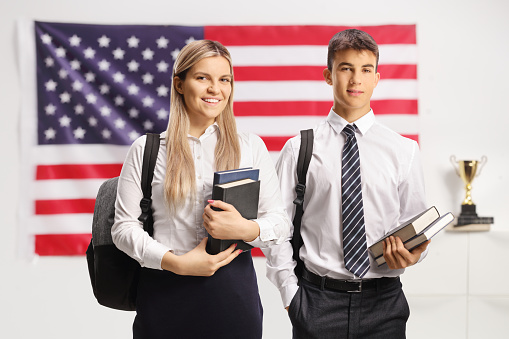 Male and female student holding books and standing in front of a USA flag