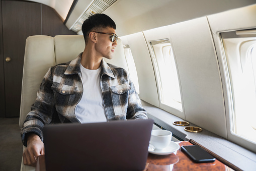 Waist-up view of early 30s corporate executive pausing from working on laptop to look out window and enjoy view while flying.