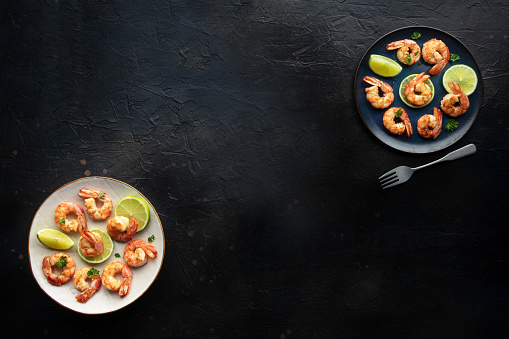Shrimps, overhead flat lay banner with copy space. Cooked shrimp with lime, shot from the top on a black slate background with a place for text