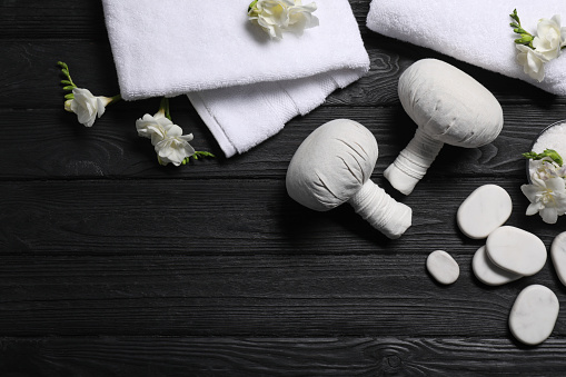 Flat lay composition with herbal massage bags and other spa products on black wooden table, space for text