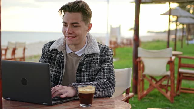 Young Man Working On Laptop In A Beach Bar In Greece