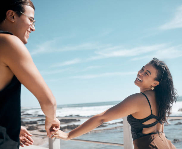 casal de amigos, rindo ou de mãos dadas na praia, mar ou mar em maquete de romance, confiança ou diversão de férias de verão. sorria, homem feliz ou mulher de ligação no local da viagem, jogo engraçado ou jogo de liberdade - trust human hand sea of hands holding - fotografias e filmes do acervo