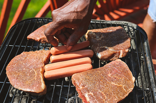 A black man putting raw meat on a charcoal grill