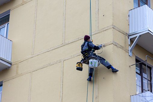 Moscow,Russia - 11 November, 2022: Worker assembler mounts iron elements on the wall of the building. Industrial climber without helmet working at height. Professional industrial mountaineering worker
