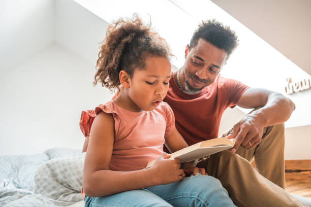 istock Mixed Race And Black Father Sitting On A Bed Reading A Book 1492313123
