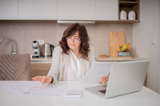 istock Mature woman using calculator while going through bills and home finances 1492313549