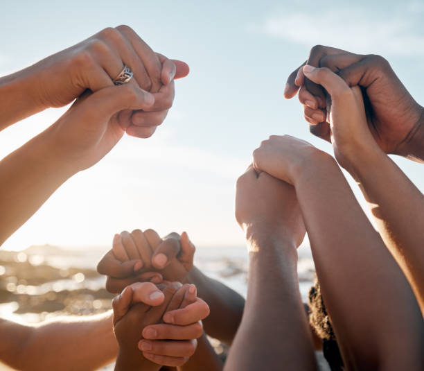 pessoas, união e mãos dadas na reunião social na praia, apoio de confiança da comunidade ou sucesso nas férias de verão. homens, mulheres e amigos da diversidade em solidariedade, formação de equipes ou metas de missão de viagem - trust human hand sea of hands holding - fotografias e filmes do acervo