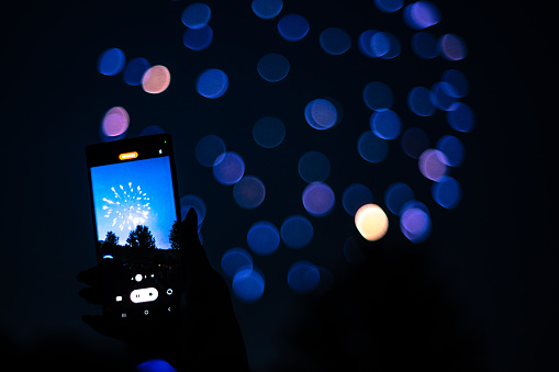 Close up of a Person holding a Cell Phone recording Fireworks firing off in the Background