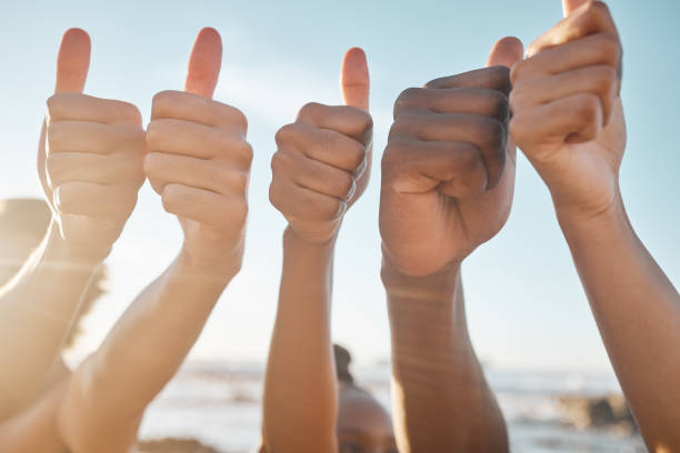 People, hands and diversity with thumbs up at beach for good job, agreement or success together. Hand of group showing thumb emoji, yes sign or like for teamwork, winning or trust in solidarity personas, manos y diversidad con pulgares hacia arriba en la playa para un buen trabajo, acuerdo o éxito juntos. mano del grupo mostrando emoji de pulgar, signo de sí o me gusta para el trabajo en equipo, ganar o confianza en la solidaridad