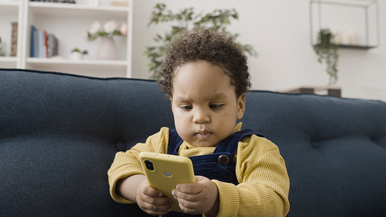 Curious African American baby playing with parent's smartphone, looking bossy