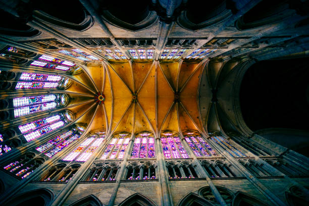 The Basilica of Saint-Denisis a large former medieval abbey church and present cathedral in the commune of Saint-Denis, a northern suburb of Paris. The church was completed in 1144 and widely considered the first structure to employ all of the elements of Gothic architecture. The image shows the ceiling and stained glass windows of that magnificant cathedral.