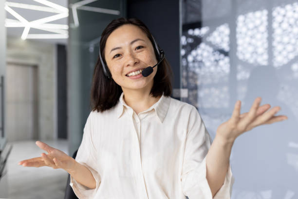 femme d’affaires avec casque d’appel vidéo souriant et regardant la caméra, femme asiatique parlant aux clients à distance, travailleur du support technique parlant, vue webcam. - hotel reception customer service representative headset receptionist photos et images de collection