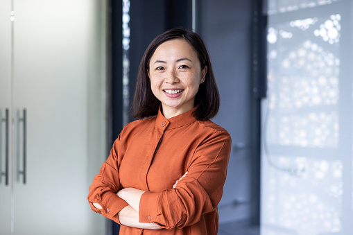 Portrait of young beautiful and successful Asian business woman, female employee smiling and looking at camera with crossed arms, financial woman satisfied with the results of her work achievement.