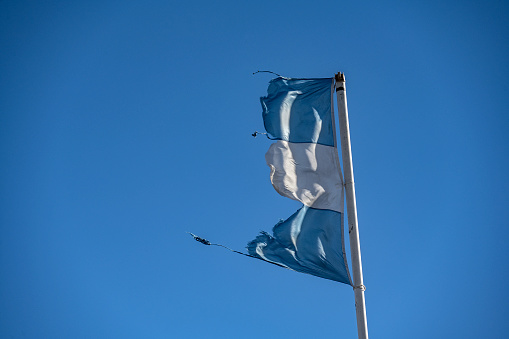 Faded Argentina flag on the mast waving in the blue sky.