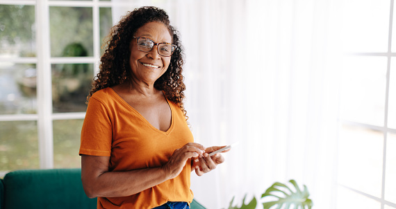 Senior woman living alone uses her smartphone to stay connected and feel secure, with the ability to make calls, send texts, and access the friendly online communities of fellow senior citizens.