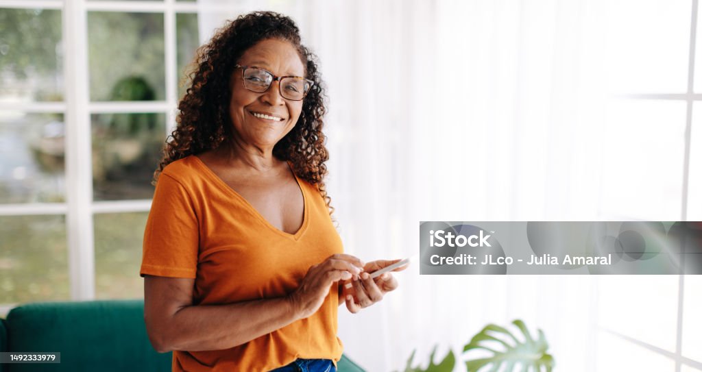 Retire senior woman living alone, using a smartphone for communication Senior woman living alone uses her smartphone to stay connected and feel secure, with the ability to make calls, send texts, and access the friendly online communities of fellow senior citizens. Senior Adult Stock Photo