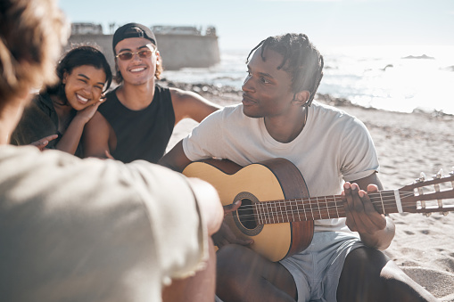 Black man, friends or playing guitar by beach, ocean or sea in holiday vacation, summer travel or social gathering. Smile, happy or couple of friends with musical instrument in relax diversity picnic