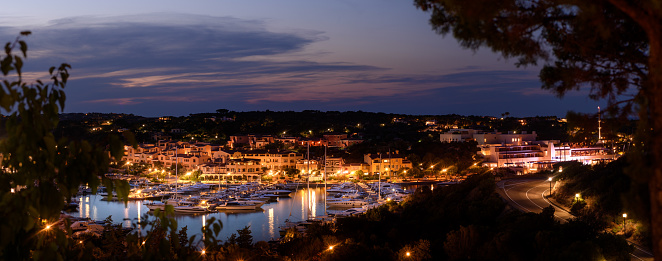 Experience the enchanting allure of Porto Cervo at night, as the lights of the village illuminate the tranquil bay. A mesmerizing display of elegance and luxury awaits in this Italian summer resort. Gaze upon the shimmering waters and be captivated by the charm of the boats dotting the bay. Discover the magical ambiance of Costa Smeralda, Sardinia, and immerse yourself in the sophisticated beauty of Porto Cervo.
