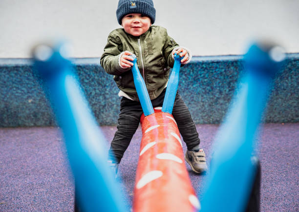 Happy child seen through the handles playing on a seesaw in a colourful playground. Playful kid outdoor on a dandle board conveys the importance of physical activity, recreation time and mental health - Indre By, Copenhagen, Denmark niño feliz visto a través de las manijas jugando en un balancín en un colorido patio de recreo. un niño juguetón al aire libre en un tablero de andle transmite la importancia de la actividad física, el tiempo de recreación y la salud mental