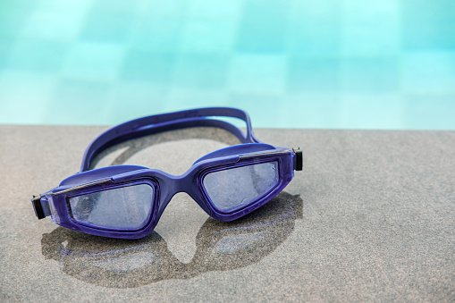 Close up Purple  Swimming glasses on poolside, Swimming health care concept,  with copy space for your text.