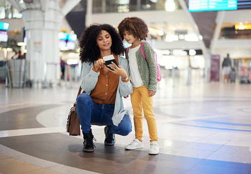 Travel, passport and mother with her child in the airport checking their boarding pass together. Trip, technology and woman browsing on a cellphone with girl kid while waiting for flight in terminal.
