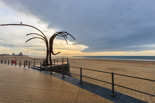 A wide strip of sand facing the North Sea borders the long Promenade Albert I in Ostend, a city in the province of West Flanders. The iron sculpture 'Dansende Golven' (Dancing Waves), work by  the artist Patrick Steen and dated 2008, welcomes the passers-by.