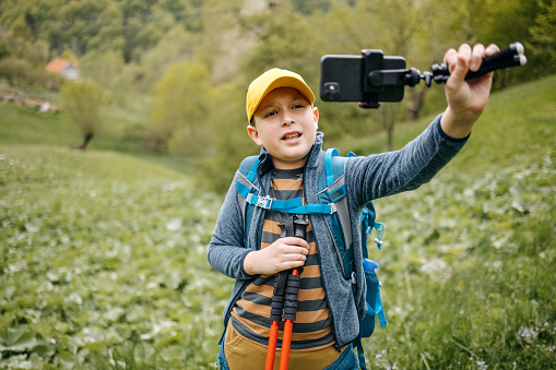 Child climbing on mountain in the spring and taking a selfie. Boy showing nature using mobile phone.