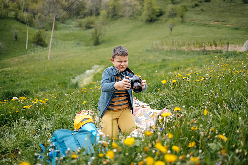 Child climbing on mountain in the spring. Boy taking a photo of flower using camera.