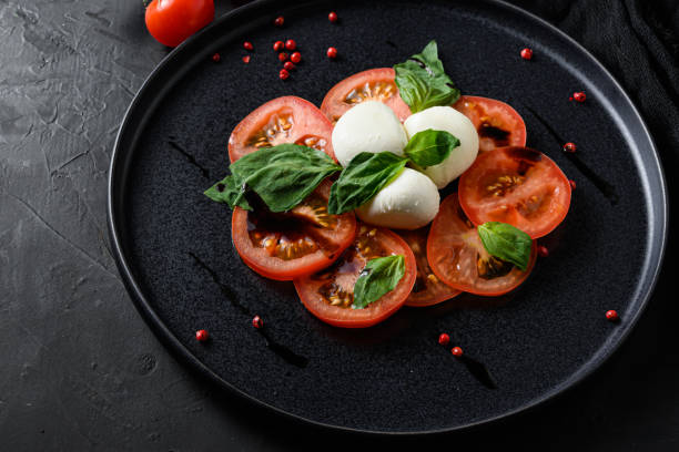 ensalada caprese concepto de cocina italiana rodajas de tomate y mozzarella con hojas de albahaca sobre platwantipasta de cerámica negra fondo de textura negra de cerca - mediterranean cuisine salad olive oil tomato salad fotografías e imágenes de stock