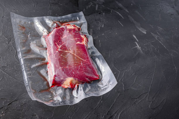 istock Rump steak in vacuum sealed bag on black textured background, side view space for text. 1492358555