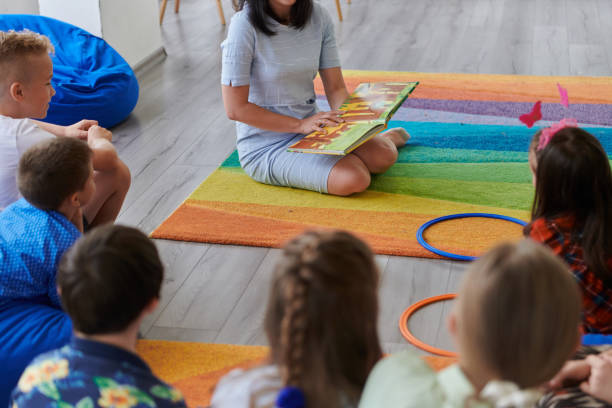istock Reading time in an elementary school or kindergarten, a teacher reading a book to children in an elementary school or kindergarten. The concept of pre-school education. Selective focus 1492359603