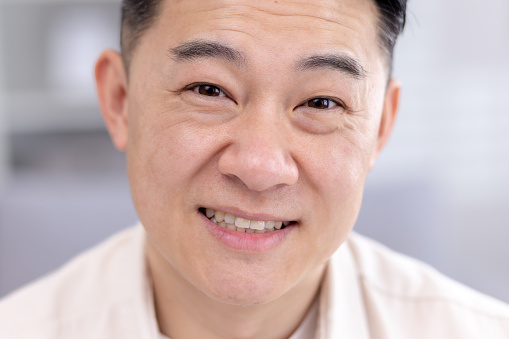 Close-up photo of an Asian man, portrait of a male businessman, looking at the camera and smiling headshot.
