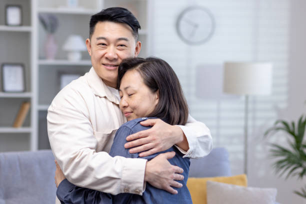 feliz casal asiático homem e mulher juntos em casa sorrindo e abraçando, família na sala de estar - japanese ethnicity heterosexual couple men smiling - fotografias e filmes do acervo