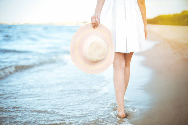 istock Young woman on a beach holding a white hat. Legs close up 1492365260