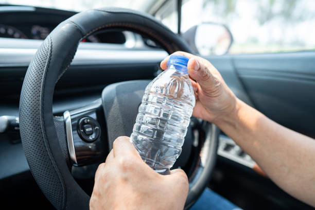 azjatycka kobieta kierowca trzymająca butelkę na wodę pitną podczas jazdy samochodem. plastikowa butelka z gorącą wodą powoduje pożar. - car fire accident land vehicle zdjęcia i obrazy z banku zdjęć