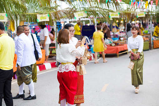 Scene with  traditionally dressed thai women at historical celebration in Phitsanulok at Traditional thai festival in street in Phitsanulok in midnorthern Thailand. People  are dressed in  traditional clothing a of history and past. Along street is a food market with traditional local thai food. Public local traditional culture event organized by local government. Women are wearing colorful clothes. In background are market stalls and some men