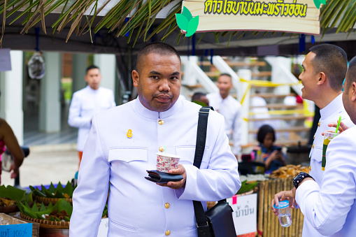 Portrait of traditionally dressed thai man with some snack at market stall on  local historical market event in Phitsanulok.  Scene at Public local traditional culture event event about history, fashion and food organized by local government. Man has very short haircut
