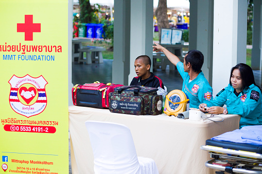 Thai Rescue workers are sitting in medical emergency area  in case of first aid . Thai ambulance staff with defibrillator on table is sitting relaxed  at Public local traditional culture event event about history, fashion and food organized by local government in Phitsanulok.  There are  two men and one woman