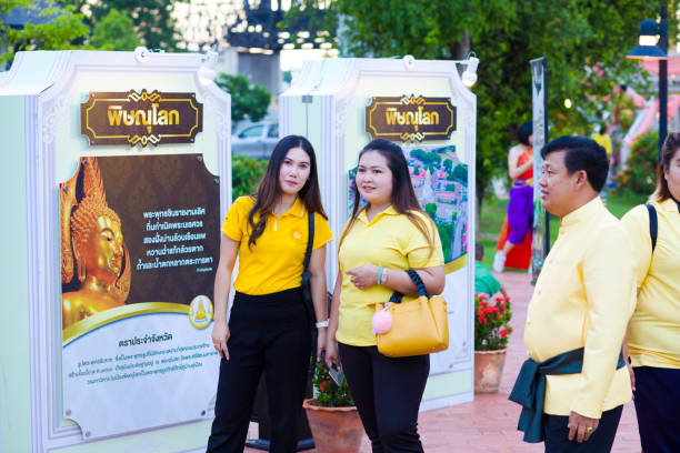 Capture of yellow dressed thai women walking  at event in Phitsanulok. Capture of yellow dressed thai women walking  at event in Phitsanulok. It is a public free local traditional culture event organized by local government. History week in Phitsanulok with traditional food, clothings and performances about history. Event  takes place at historical grounds of Wat Wihan Thong Historical Site near Nan river and is local way of keeping history alive. At right side are a man and more people. In background are billboards true thailand classic stock pictures, royalty-free photos & images