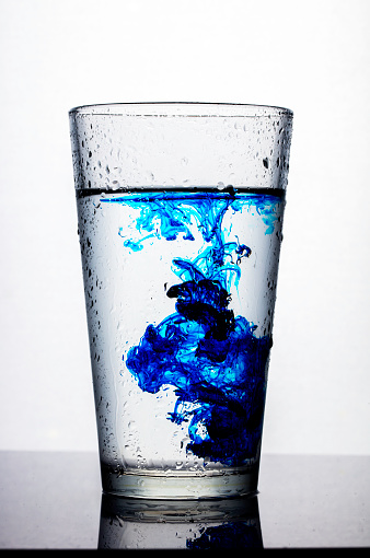 Glass of water with blue color drops