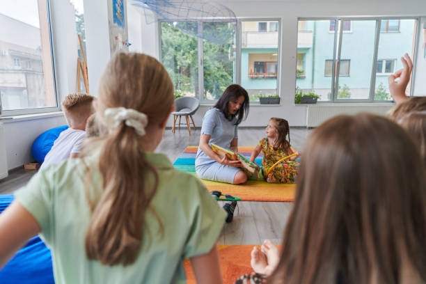 istock Reading time in an elementary school or kindergarten, a teacher reading a book to children in an elementary school or kindergarten. The concept of pre-school education. Selective focus 1492370977