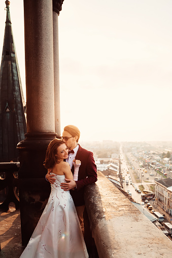 The groom hugs and gently kisses her woman on the balcony on the background of the city