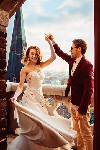 A smiling bride dances with her beloved husband on the balcony of an old building