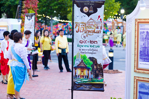 Scene at public free local traditional culture event organized by local government in Phitsanulok. Traditionally dressed thai people walking between  historical images at event in Phitsanulok. History week in Phitsanulok with traditional food, clothings and performances about history. Event  takes place at historical grounds of Wat Wihan Thong Historical Site near Nan river and is local way of keeping history alive.