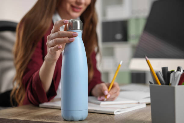 Woman holding thermos bottle at workplace, closeup Woman holding thermos bottle at workplace, closeup blue reusable water bottle stock pictures, royalty-free photos & images