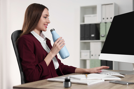 Woman holding light blue thermos bottle at workplace