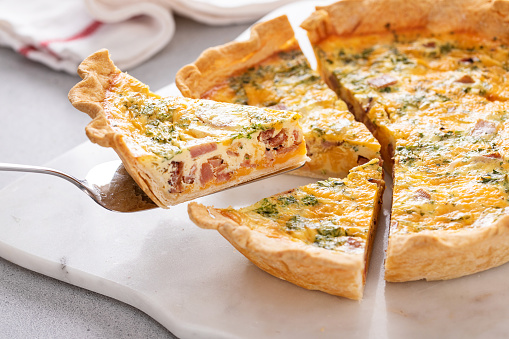 Homemade quiche with ham, cheddar cheese and parsley cut on the table with a slice taken out